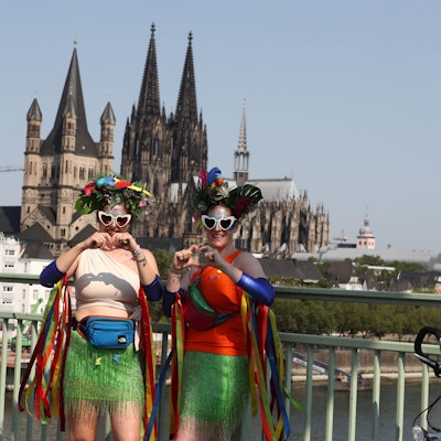 Zwei Damen formen Herzen mit ihren Händen. Im Hintergrund der Kölner Dom.