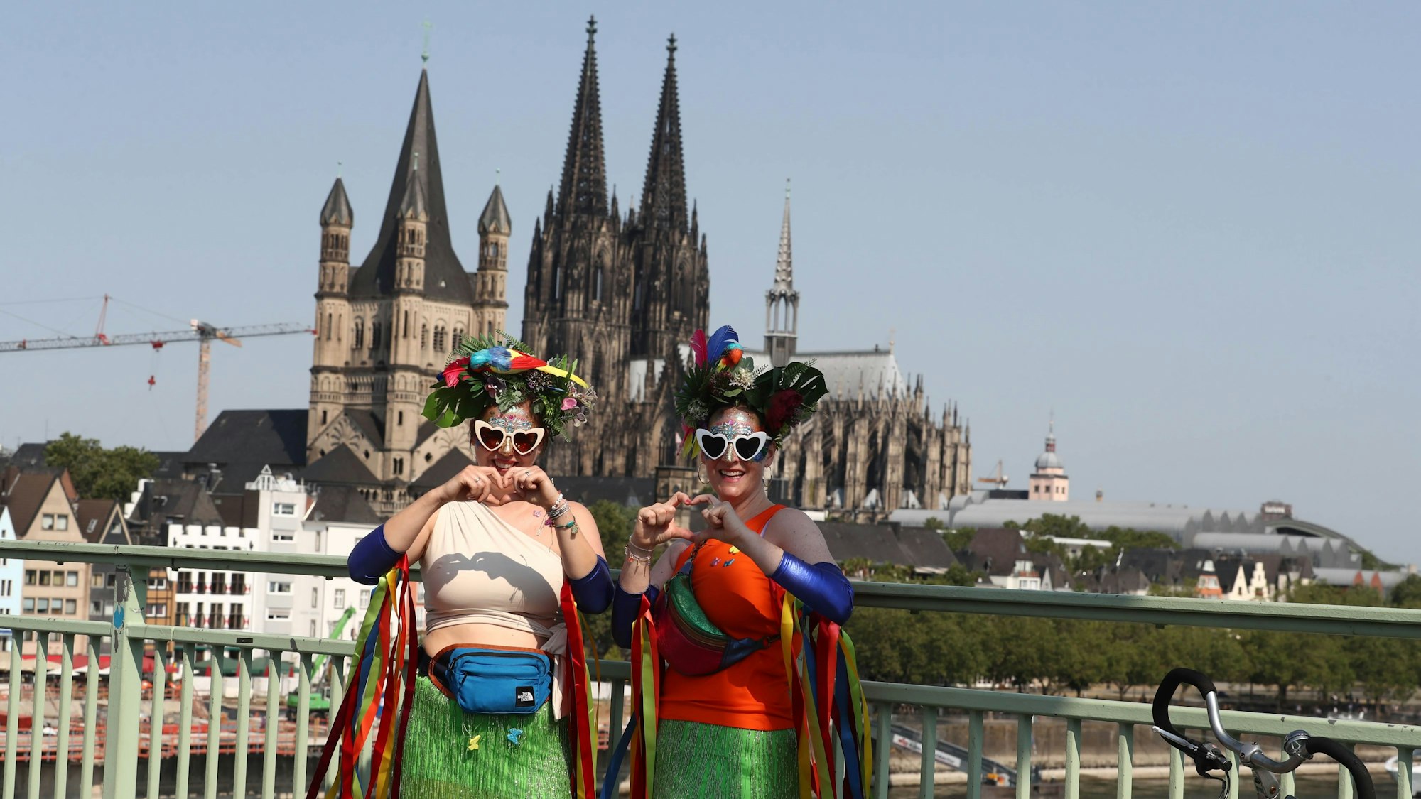 Zwei Damen formen Herzen mit ihren Händen. Im Hintergrund der Kölner Dom.