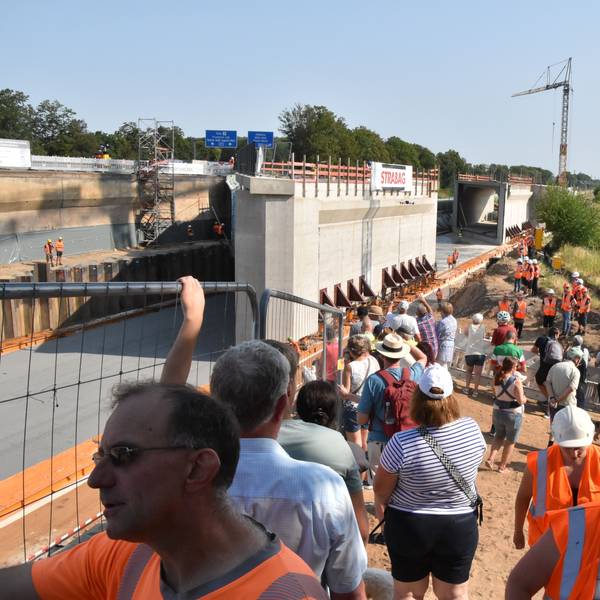 An der Baustelle stehen Anwohner Bahn- und Firmenmitarbeiter, im Hintergrund die 9000 Tonnen schweren Brückenbauteile..