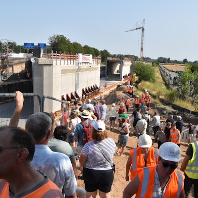 An der Baustelle stehen Anwohner Bahn- und Firmenmitarbeiter, im Hintergrund die 9000 Tonnen schweren Brückenbauteile..