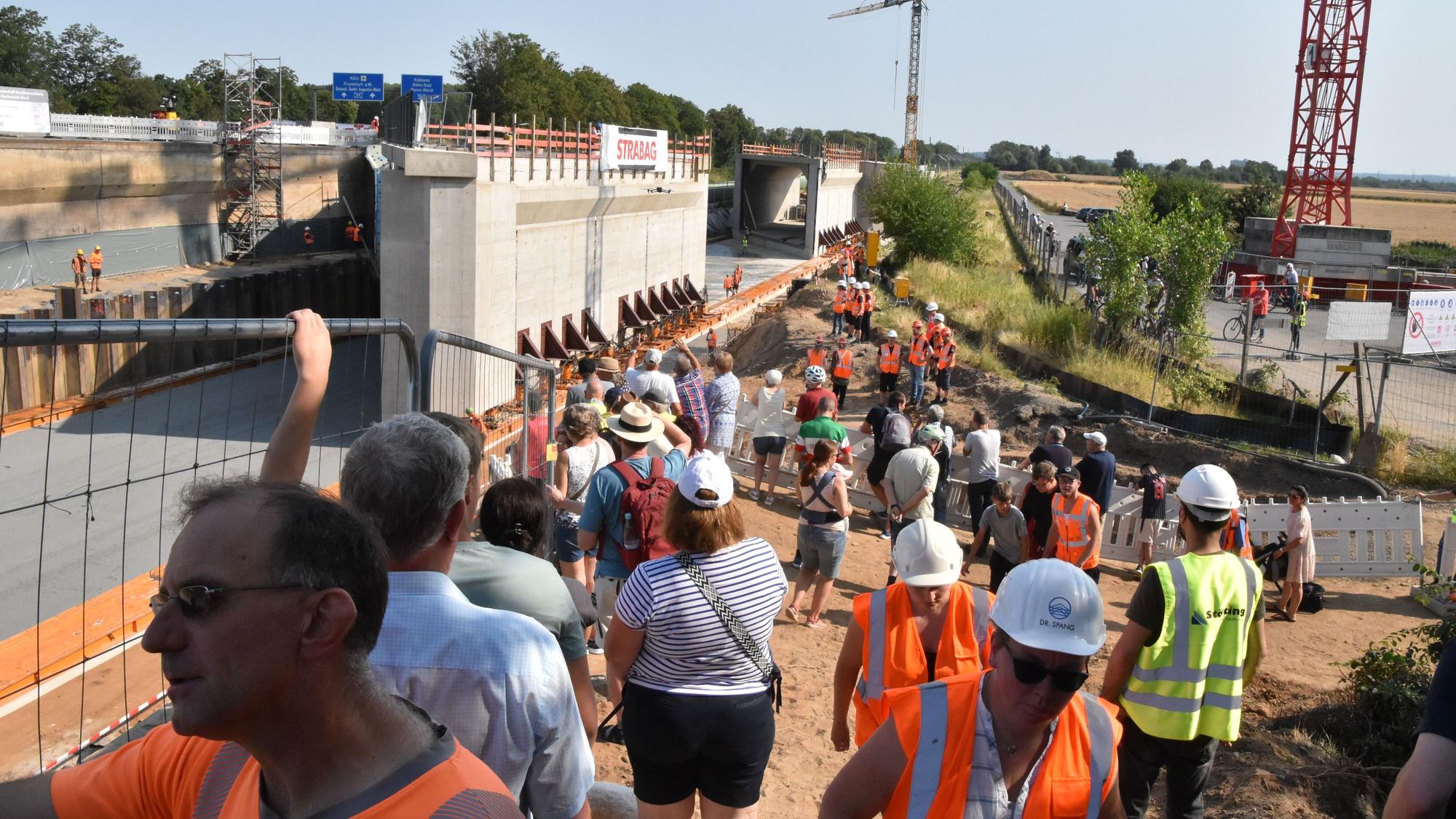 An der Baustelle stehen Anwohner Bahn- und Firmenmitarbeiter, im Hintergrund die 9000 Tonnen schweren Brückenbauteile..