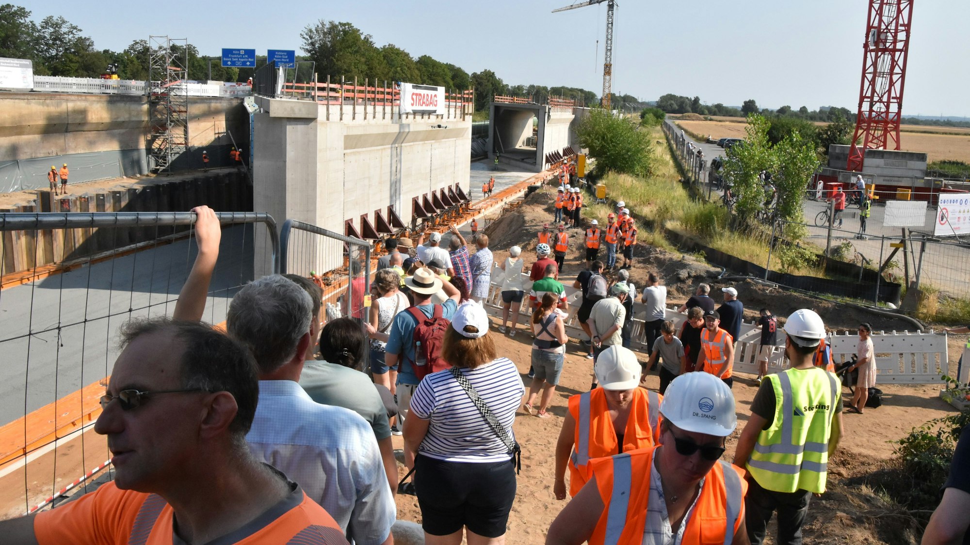 An der Baustelle stehen Anwohner Bahn- und Firmenmitarbeiter, im Hintergrund die 9000 Tonnen schweren Brückenbauteile..