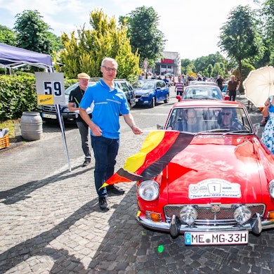 Lindlars Bürgermeister schwenkt die Startflagge bei der Abfahrt zur ADAC-Oldtimer-Rallye.