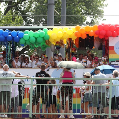 Ein Bus, der mit Luftballons in Regenbogenfarben geschmückt ist, fährt an Zuschauenden vorbei.