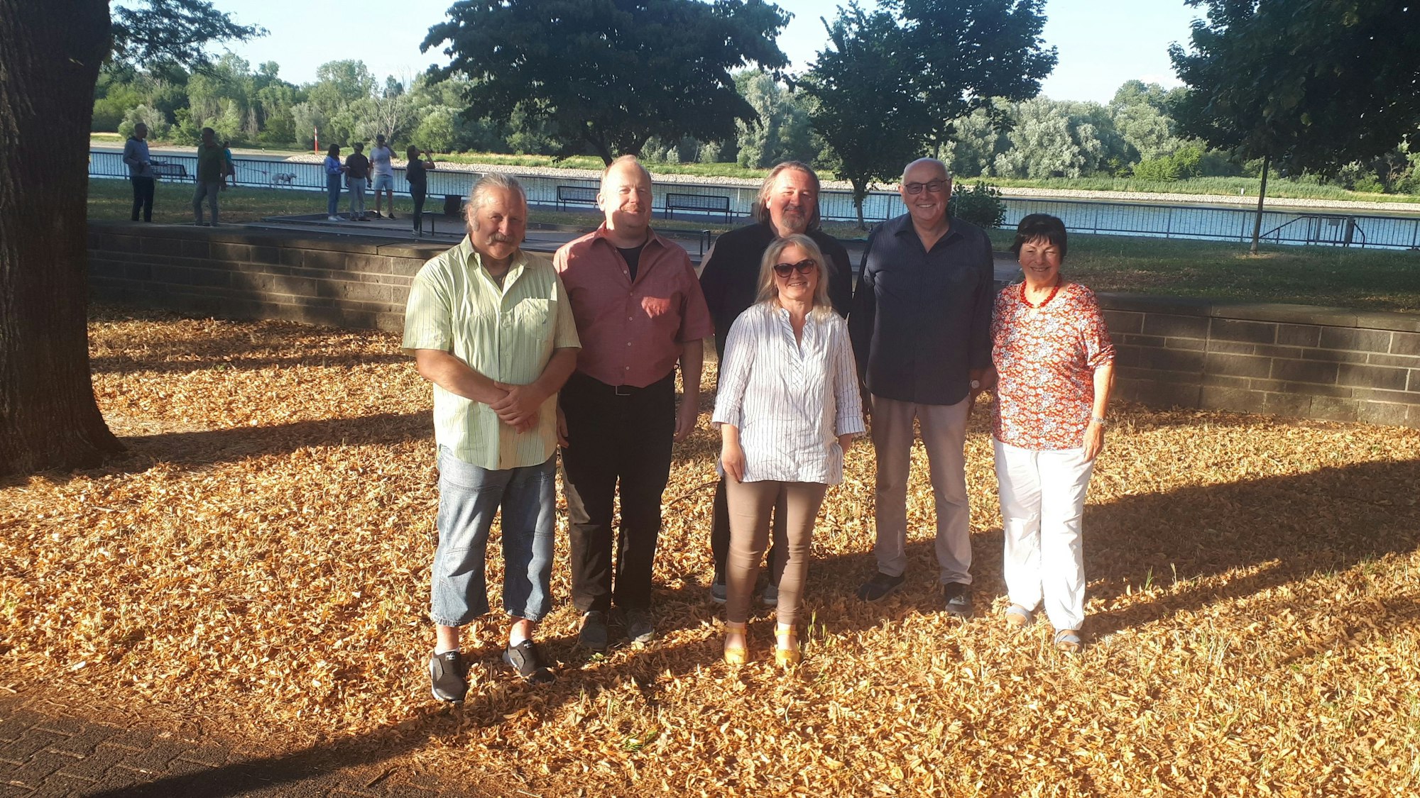 Vier Männer und zwei Frauen stehen unter einem Baum, im Hintergrund ist der Rhein zu sehen.