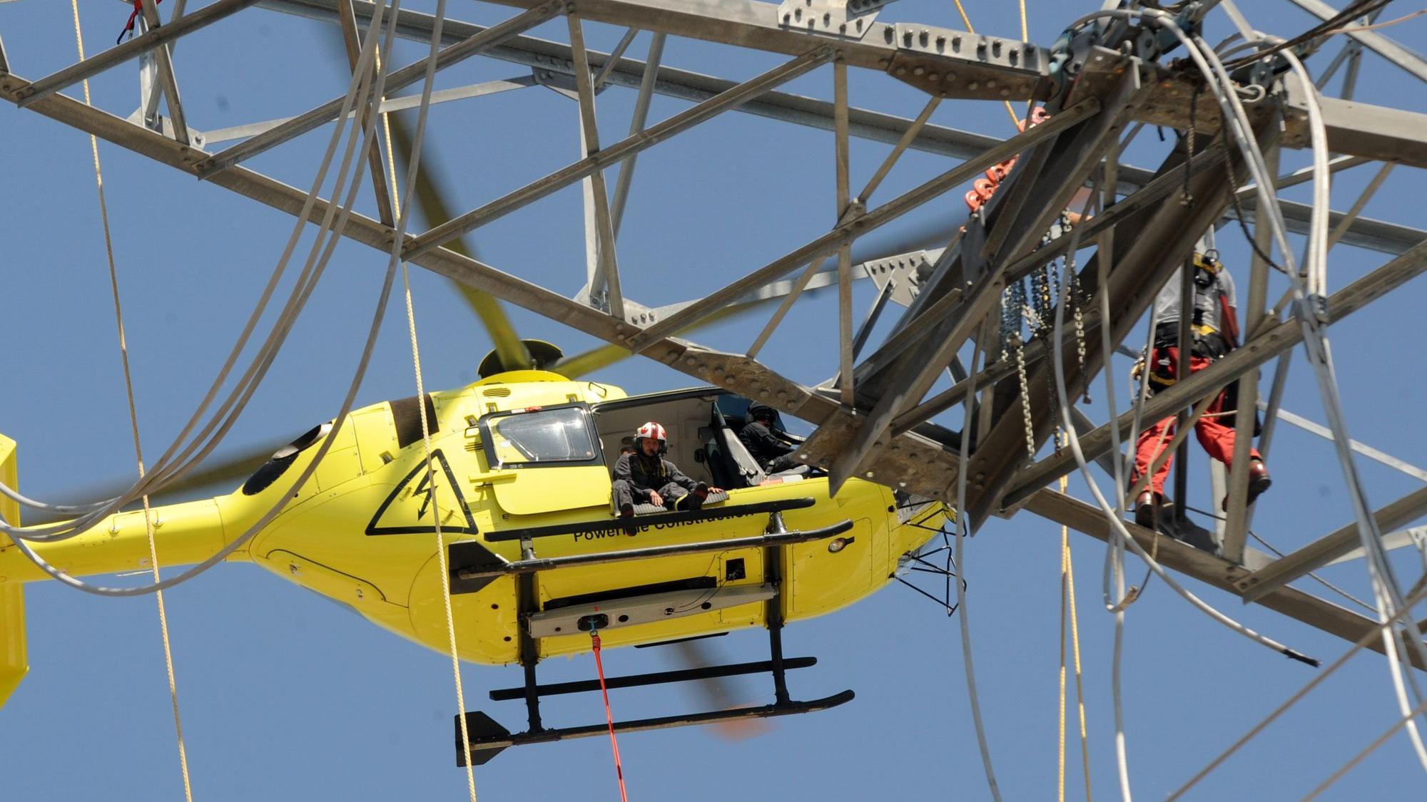Das Bild zeigt einen Hubschrauber vor dem Ausleger eines Strommastes.