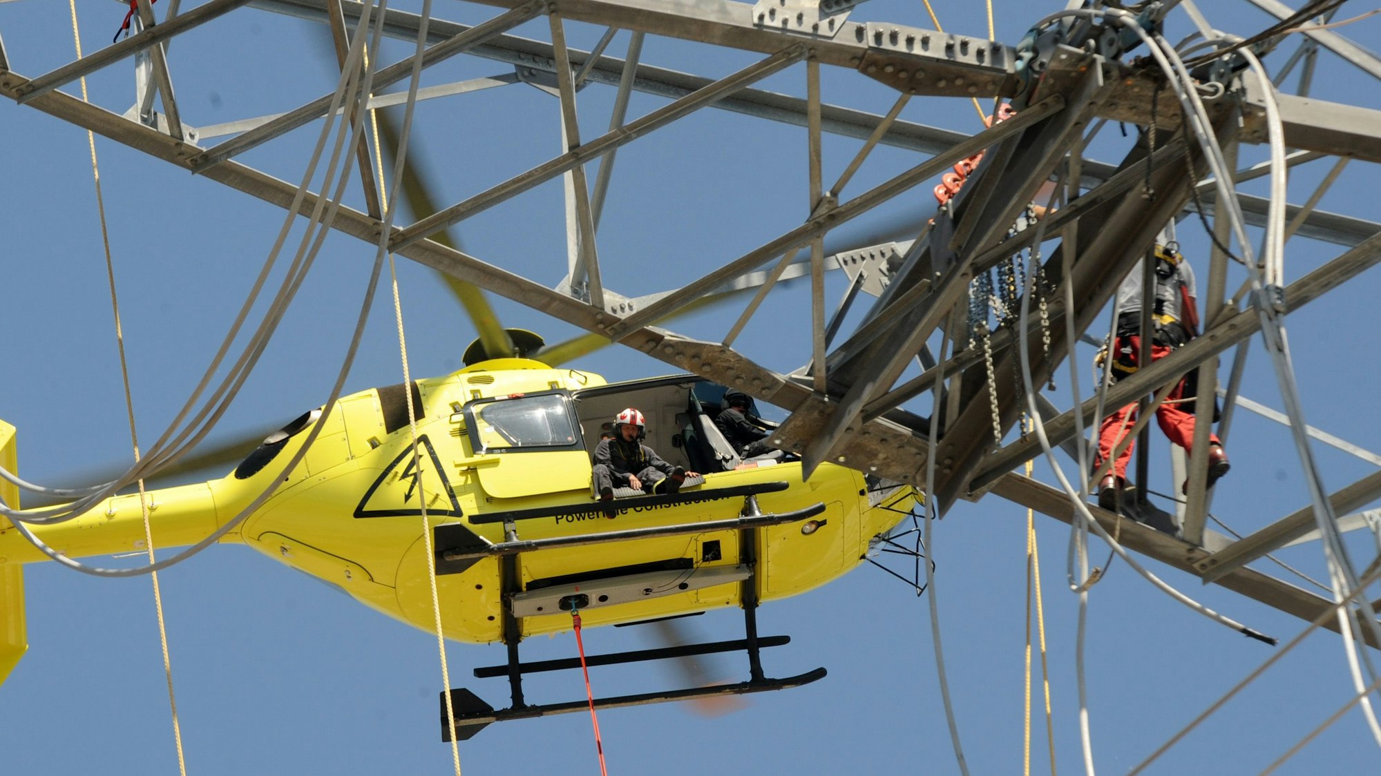 Das Bild zeigt einen Hubschrauber vor dem Ausleger eines Strommastes.