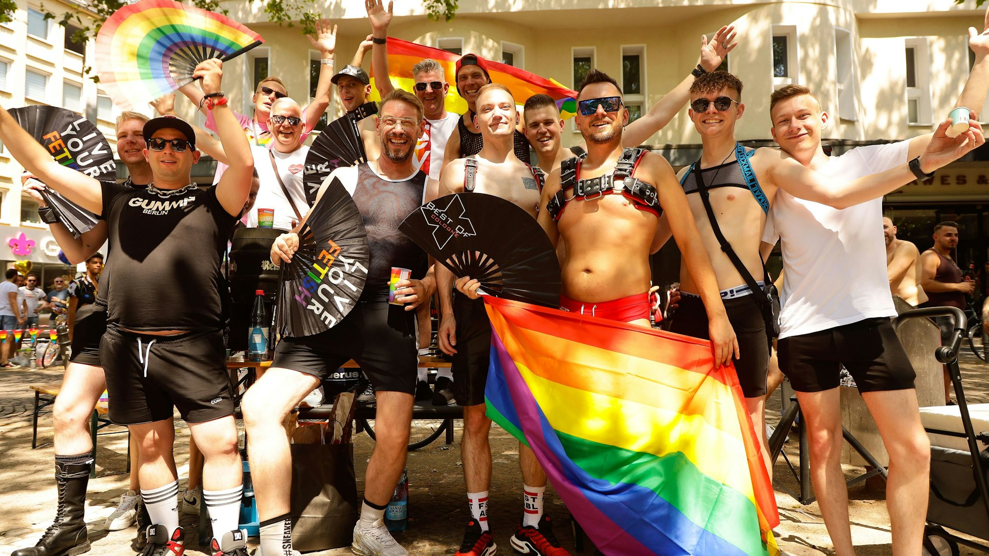 Eine Gruppe von Menschen steht mit Regenbogen-Fahnen am Rand der CSD-Parade.