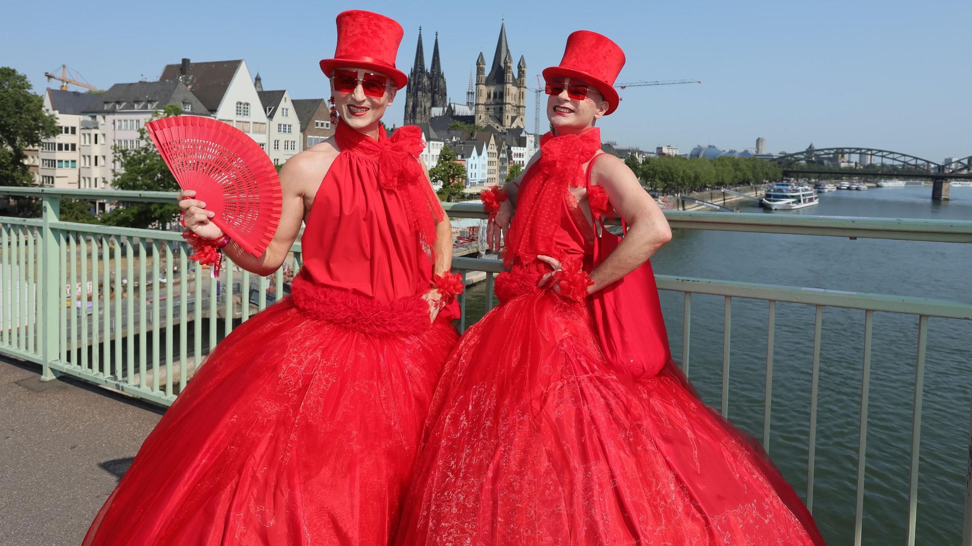 Zwei in Rot gekleidete Teilnehmende an der CSD-Parade stehen auf der Deutzer Brücke