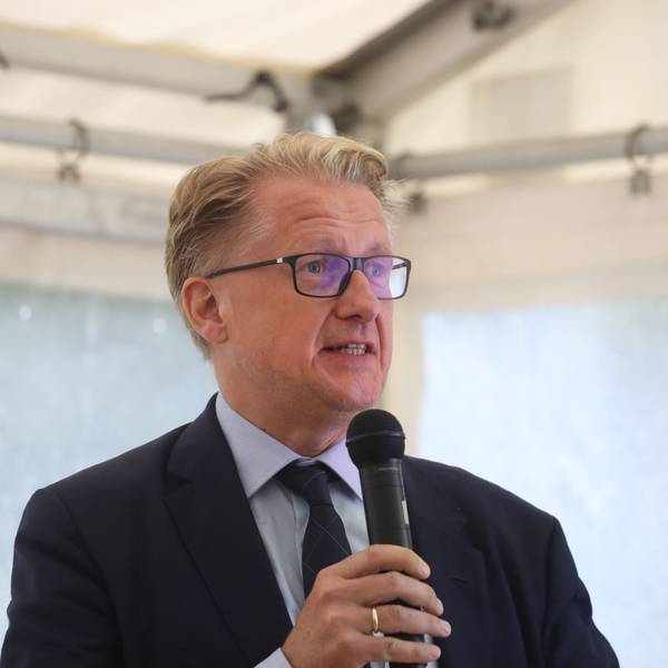 Ein Mann mit blonden Haaren und Brille hat ein Mikrofon in der Hand.