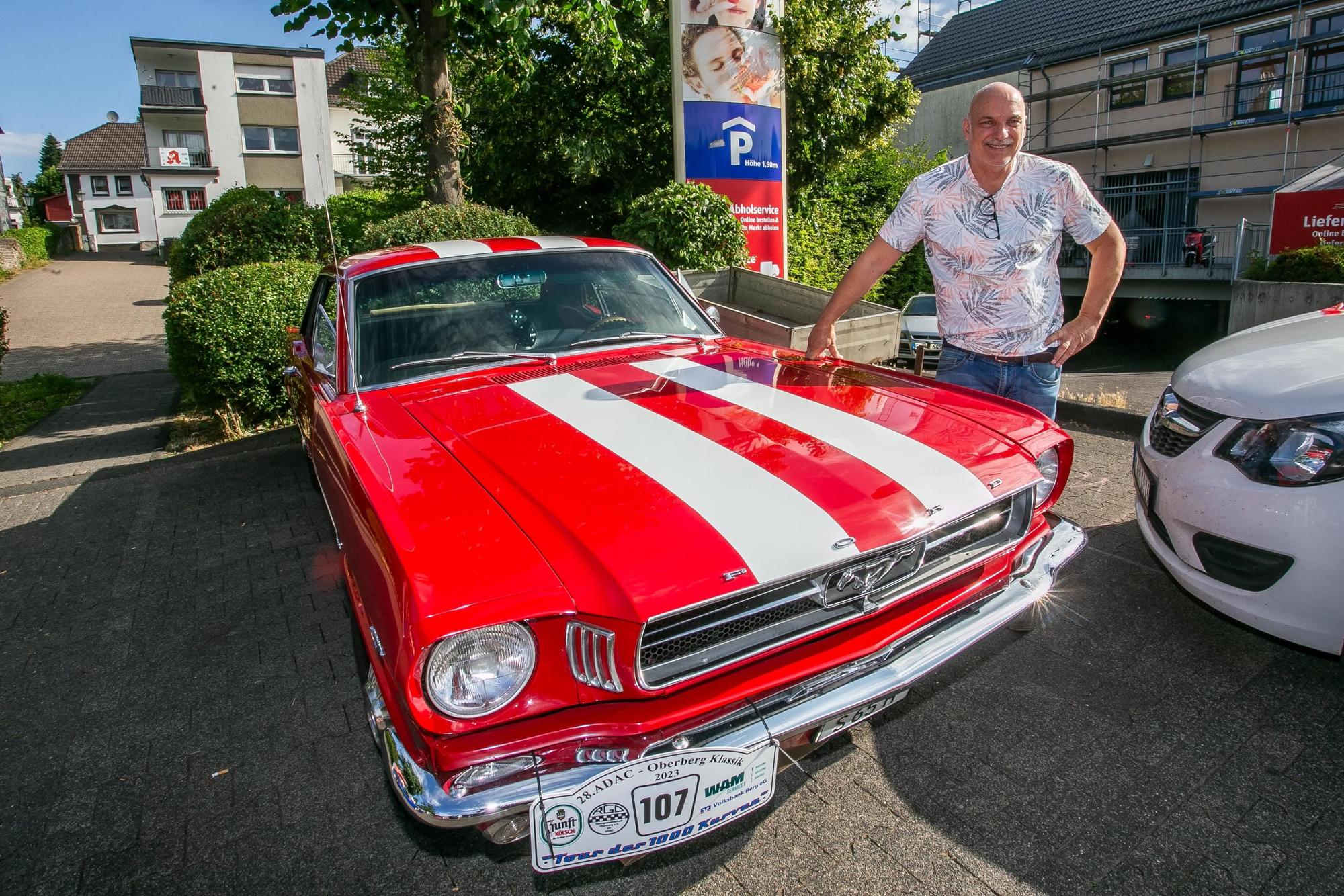Stephan Schüller steht an der Motorhaube seines rot-weißen Ford Mustang.