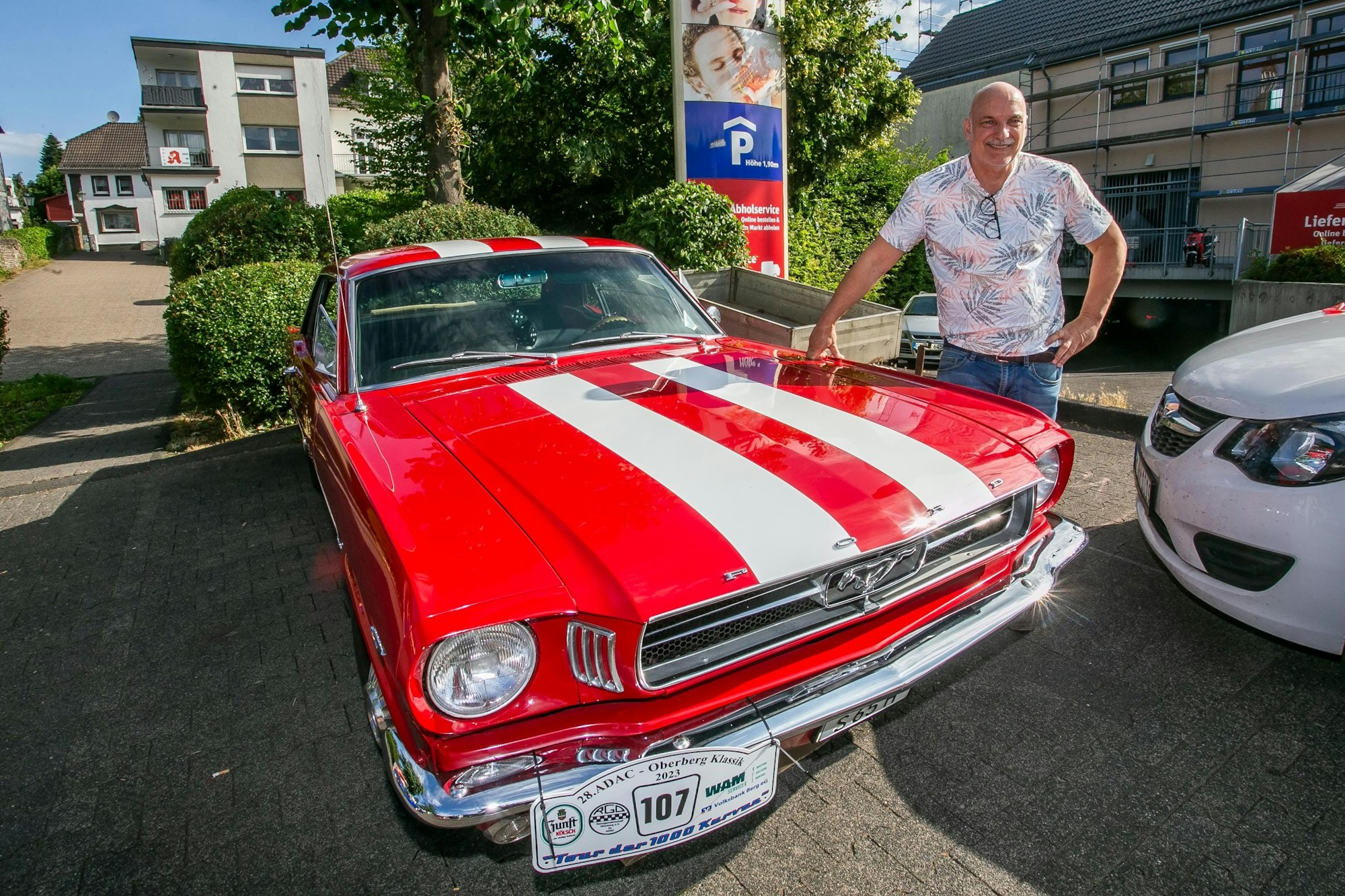 Stephan Schüller steht an der Motorhaube seines rot-weißen Ford Mustang.