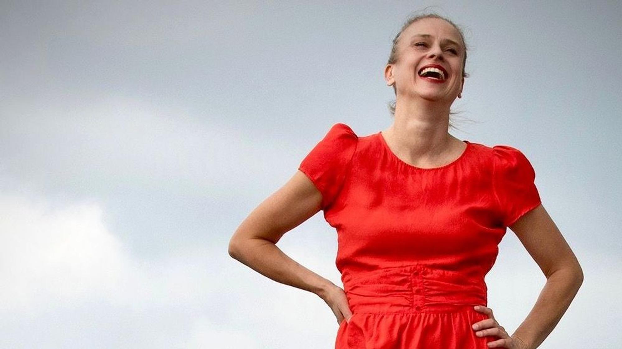 Melanie Haupt trägt ein rotes Kleid und lacht, der Himmel ist grau.