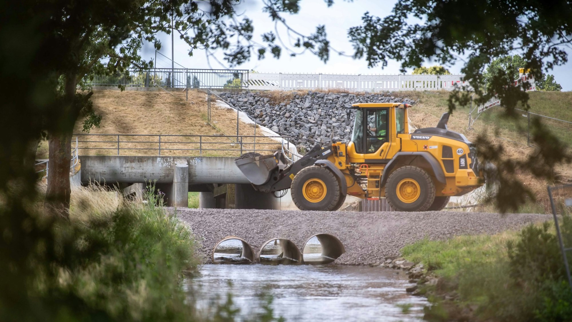 Mit einem gelben Radlader wird am Hochwasserrückhaltebecken bei Horchheim gearbeitet. Das Foto ist durch eine Böschung hindurch aufgenommen worden.