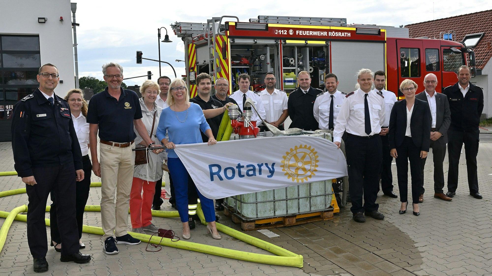 Alle stehen zusammen vor einem Feuerwehrauto und grinsen in die Kamera.