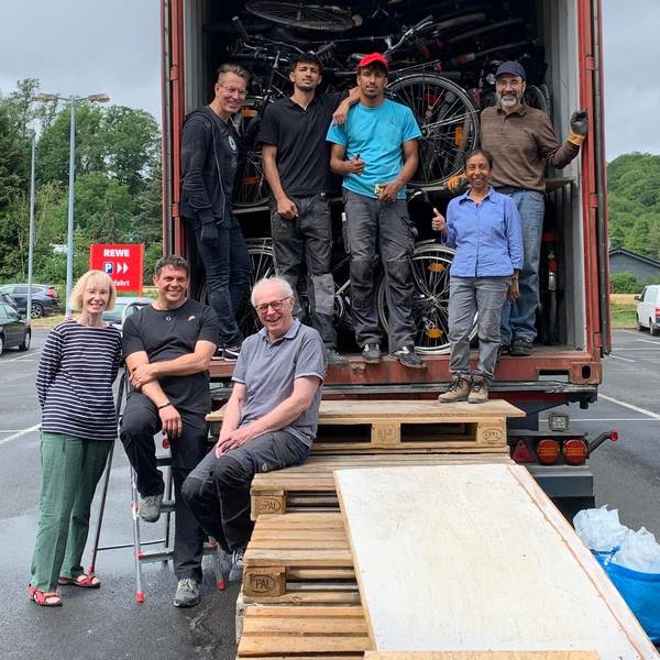 Eine Gruppe von Menschen steht vor einem mit Fahrrädern voll beladenem Container.