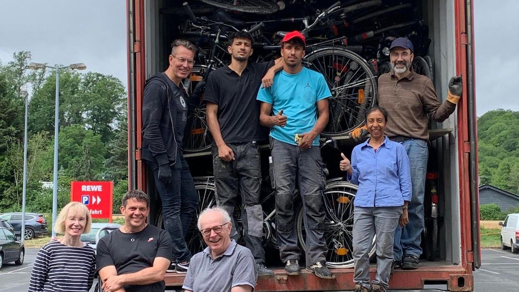 Eine Gruppe von Menschen steht vor einem mit Fahrrädern voll beladenem Container.