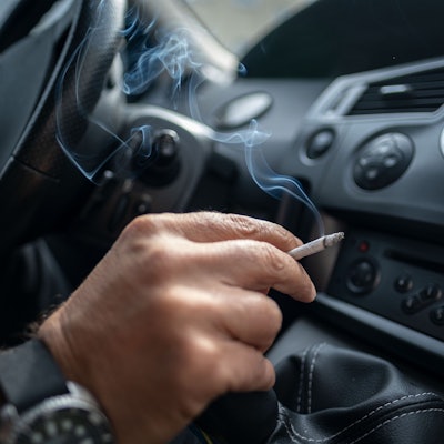 Ein Mann sitzt rauchend am Lenkrad eines Autos.