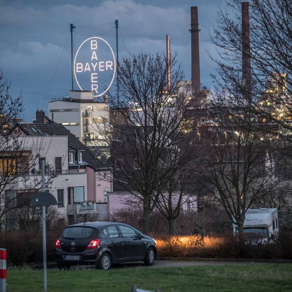 Vorne Autos und Häuser, hinten das Bayer-Kreuz in der Dämmerung.
