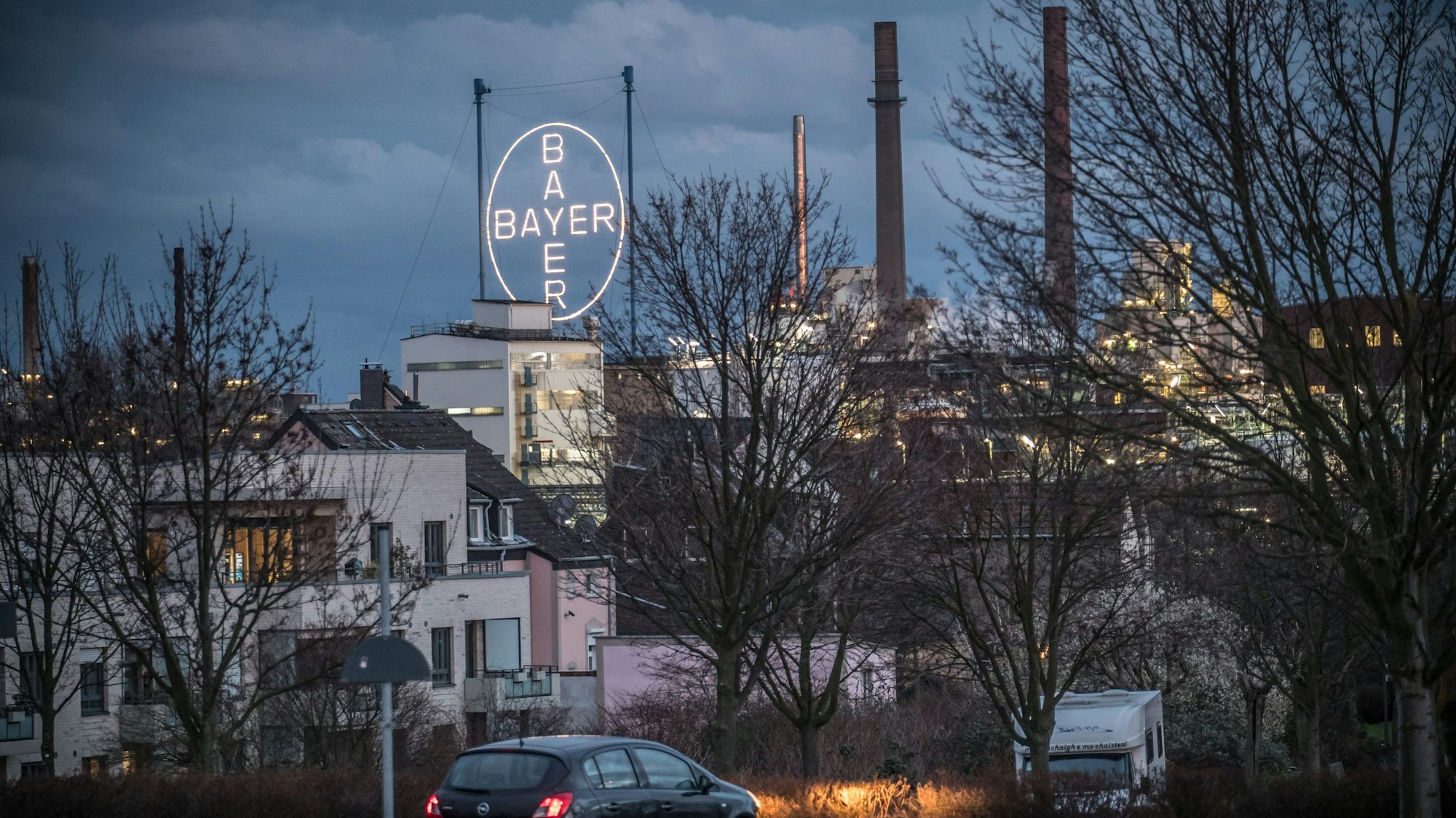 Vorne Autos und Häuser, hinten das Bayer-Kreuz in der Dämmerung.