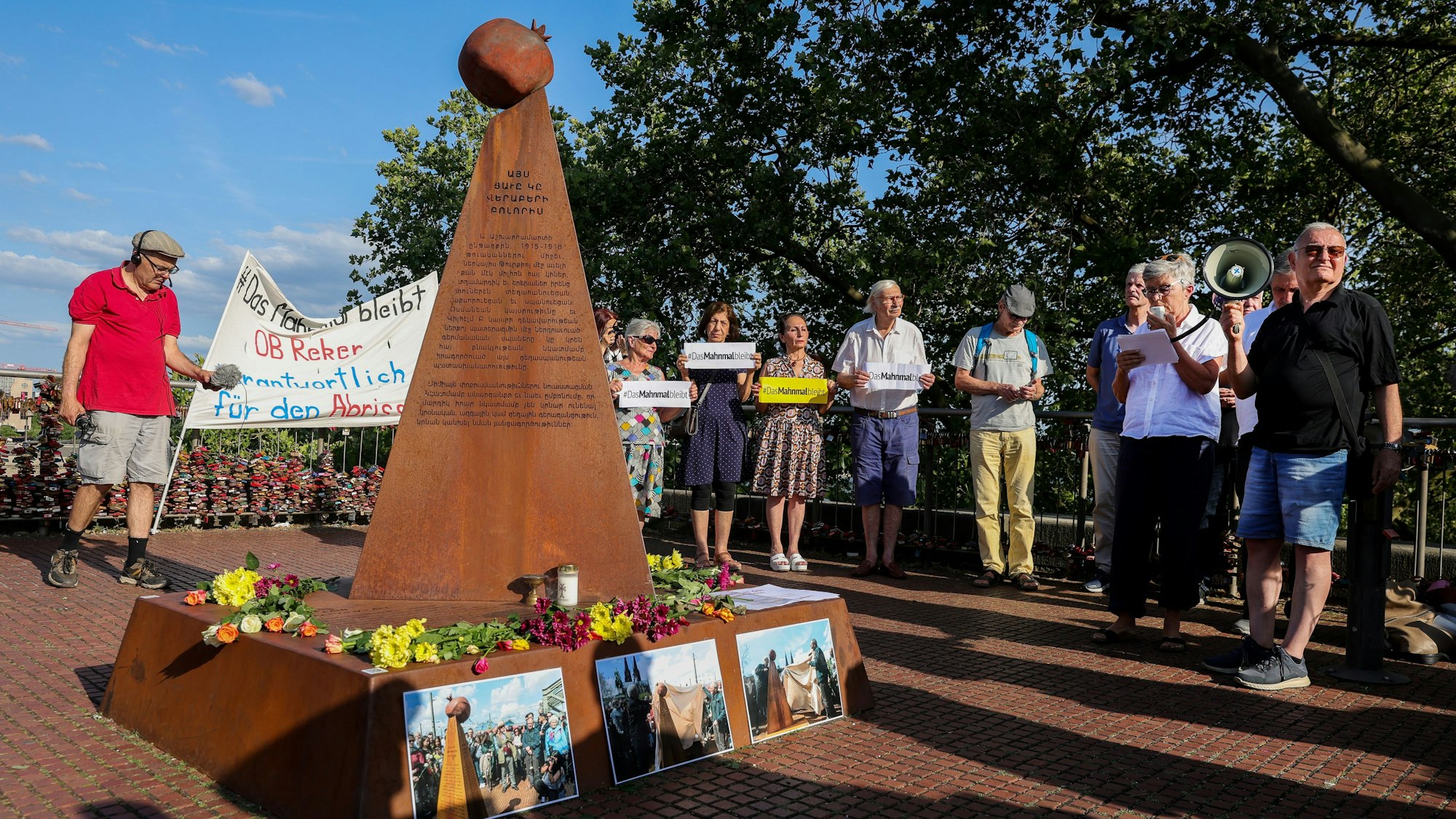 Zwölf Menschen demonstrieren mit Plakaten in der Hand um das armenische Denkmal an der Kölner Hohenzollernbrücke gegen dessen erzwungenen Abbau.
