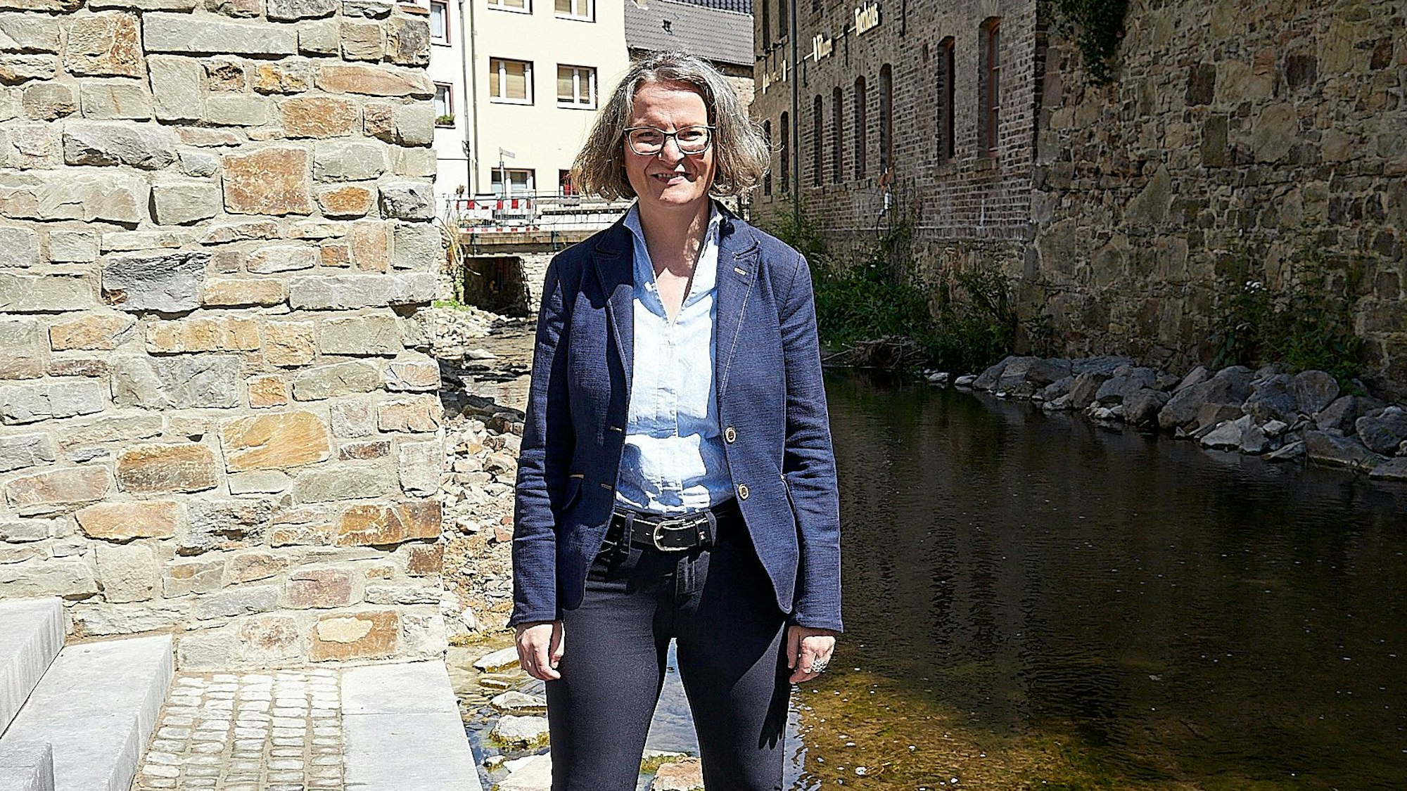 Ina Scharrenbach steht an der Erft in Bad Münstereifel an einem sonnigen Tag auf einer Treppe.