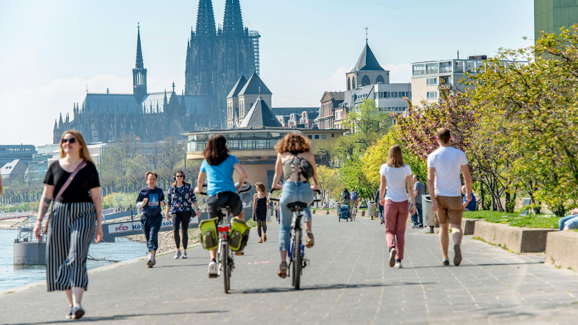 Mehrere Fußgängerinnen und Fußgänger teilen sich das schmale Konrad-Adenauer-Ufer in Köln, im Hintergrund ist die Bastei zu sehen.