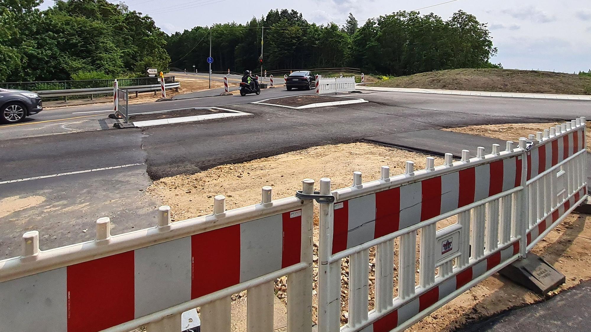Das Bild zeigt eine frisch asphaltierte Straße, die oberste Asphaltschicht fehlt noch. Im Vordergrund stehen rot-weiße Warnbaken.