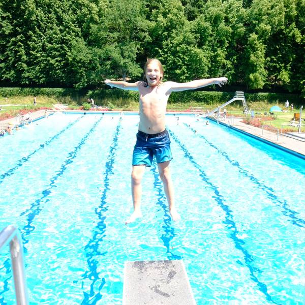 Ein Junge springt rückwärts vom Drei-Meter-Brett, im Hintergrund ist das Schwimmbecken zu sehen.