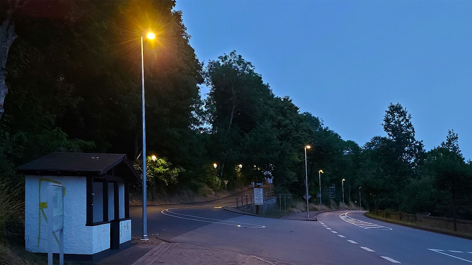 Das Bild zeigt die Ortsdurchfahrt Kronenburg in der Abenddämmerung. Die neuen Straßenlampen sind bereits eingeschaltet.