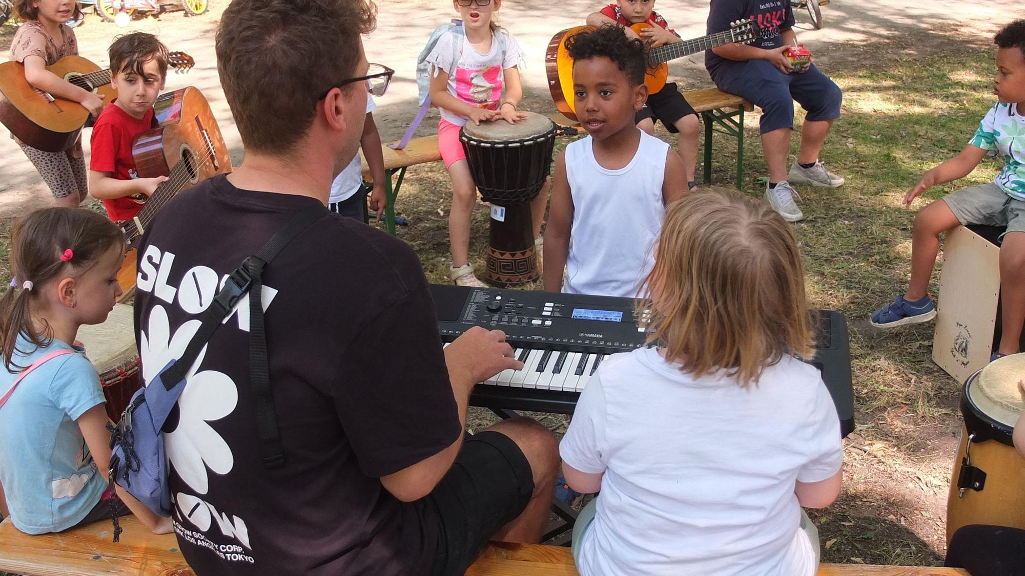Kinder stehen und sitzen um einen Mann, der auf einem Keyboard spielt.