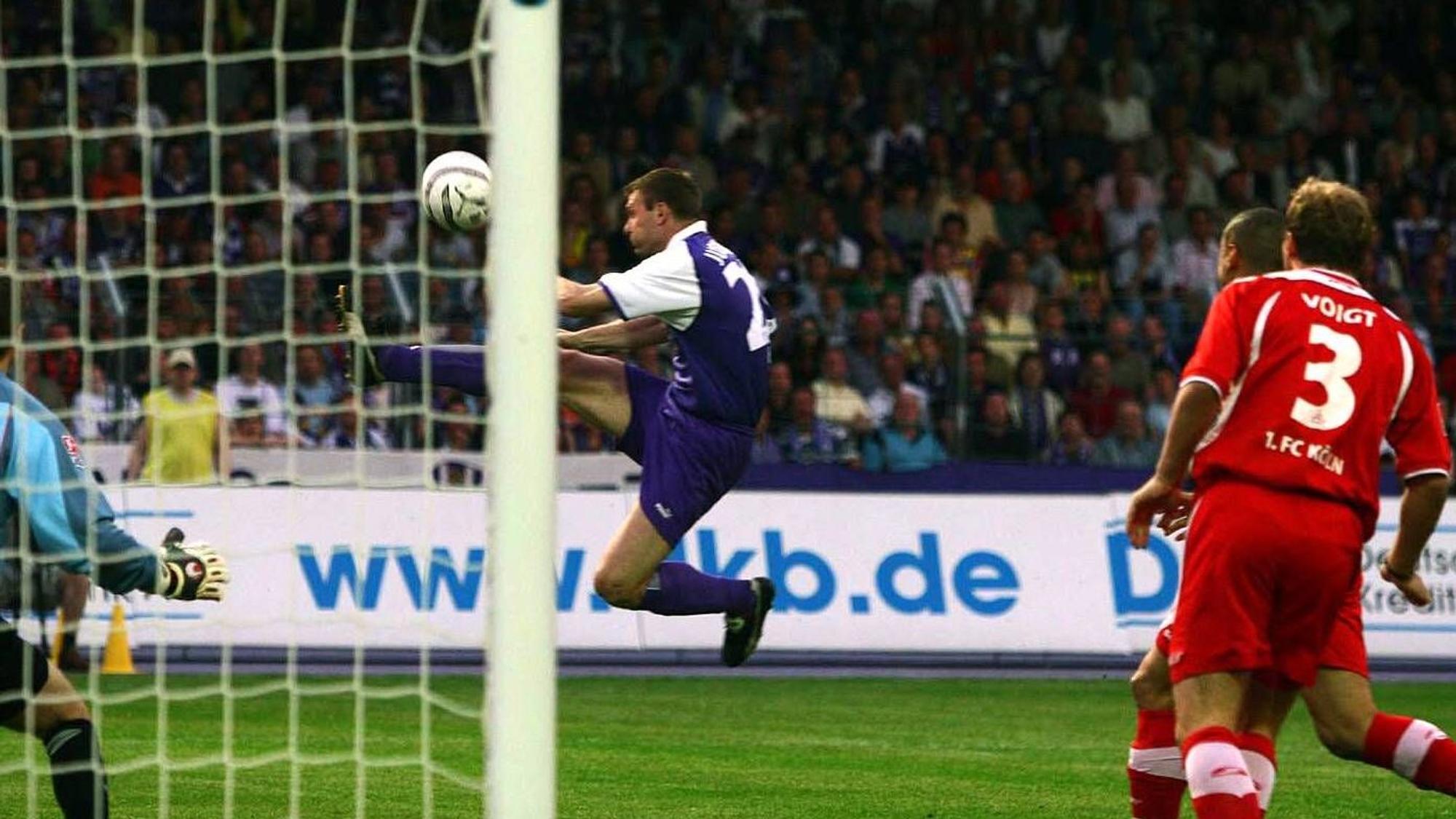 Der Stürmer Andrzej Juskowiak vom FC Erzgebirge Aue springt in der Bildmitte artistisch dem Ball hinterher. Ein Verteidiger des 1. FC Köln kann nur zusehen.