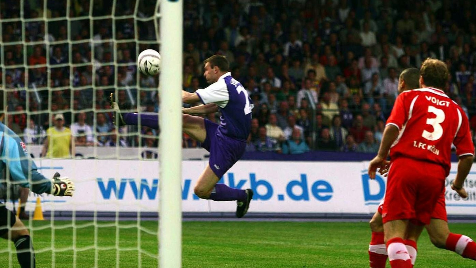 Der Stürmer Andrzej Juskowiak vom FC Erzgebirge Aue springt in der Bildmitte artistisch dem Ball hinterher. Ein Verteidiger des 1. FC Köln kann nur zusehen.