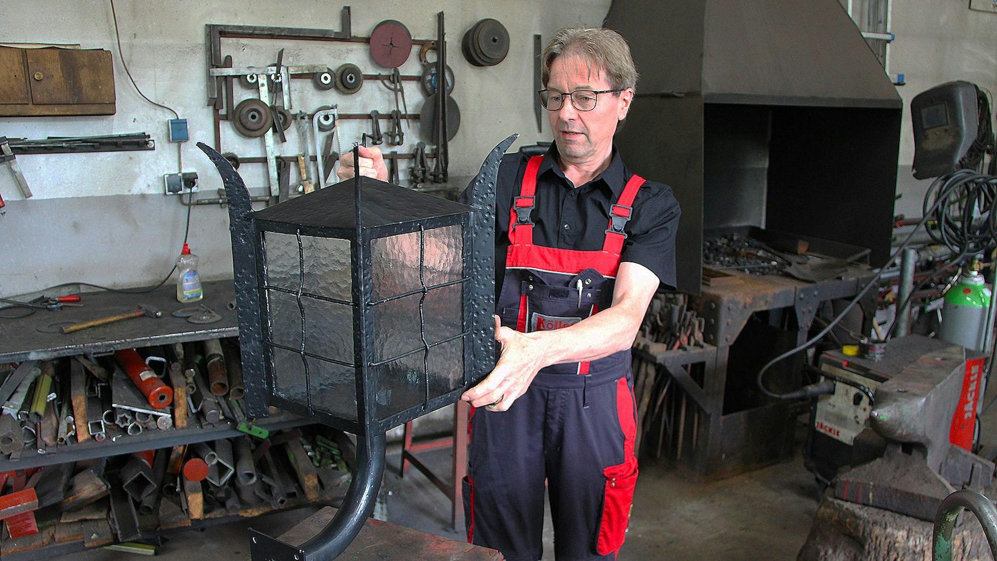Das Bild zeigt Schmied Albert Köller in seiner Werkstatt. Er hat eine große Lampe in der Hand.