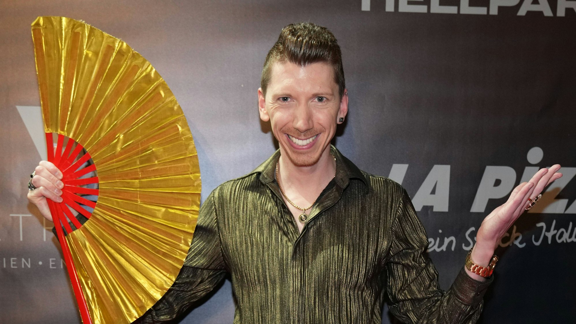 Manuel Flickinger auf der All Together Charity-Gala 2023. Er hält einen großen goldenen Fächer in der Hand.