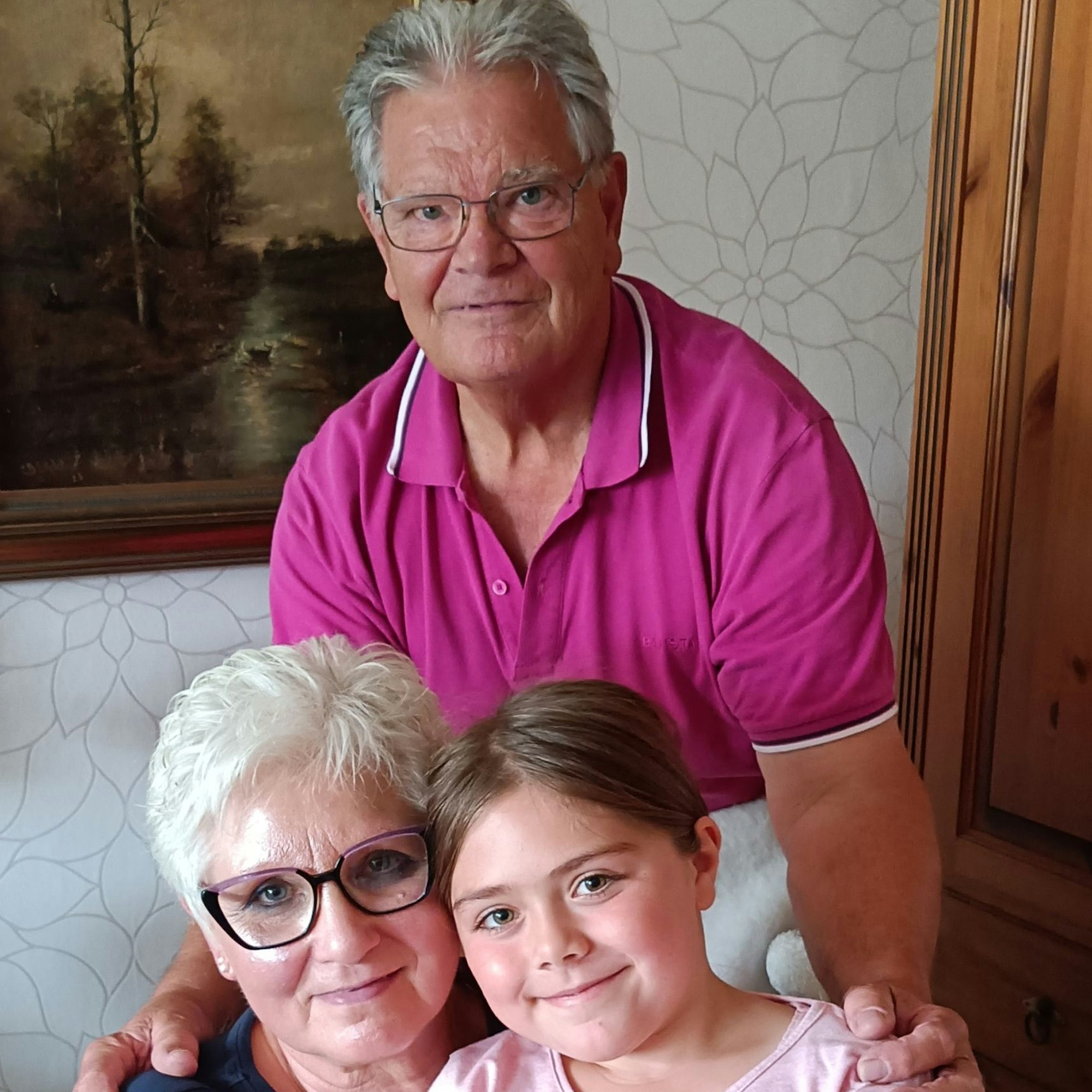 Josef und Agnes Pempe in ihrem Wohnzimmer. Agnes hat Enkelin Anna auf dem Schoß, Josef steht hinter beiden und hat die Hände auf ihren Schultern.