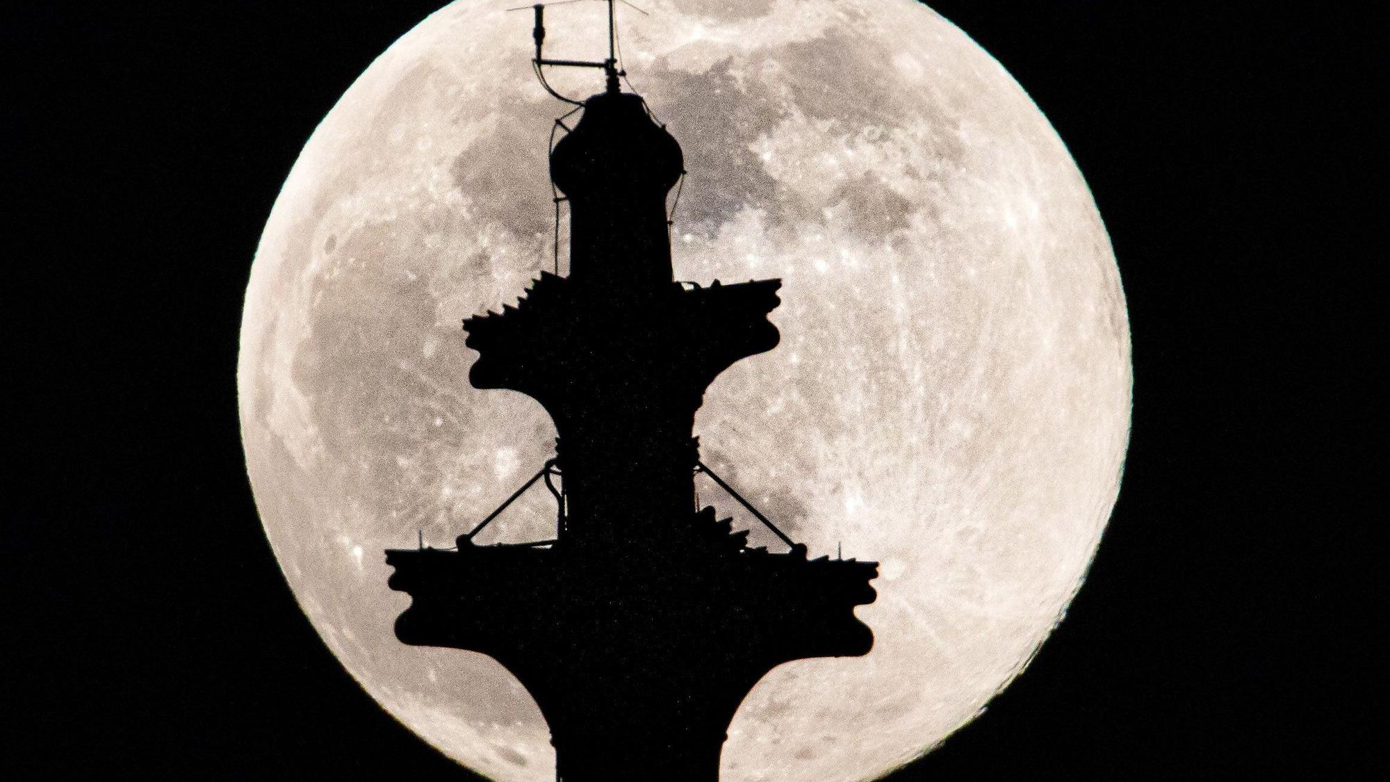 Der Vollmond steht hinter der Kreuzblume auf dem Nordturm des Kölner Doms.