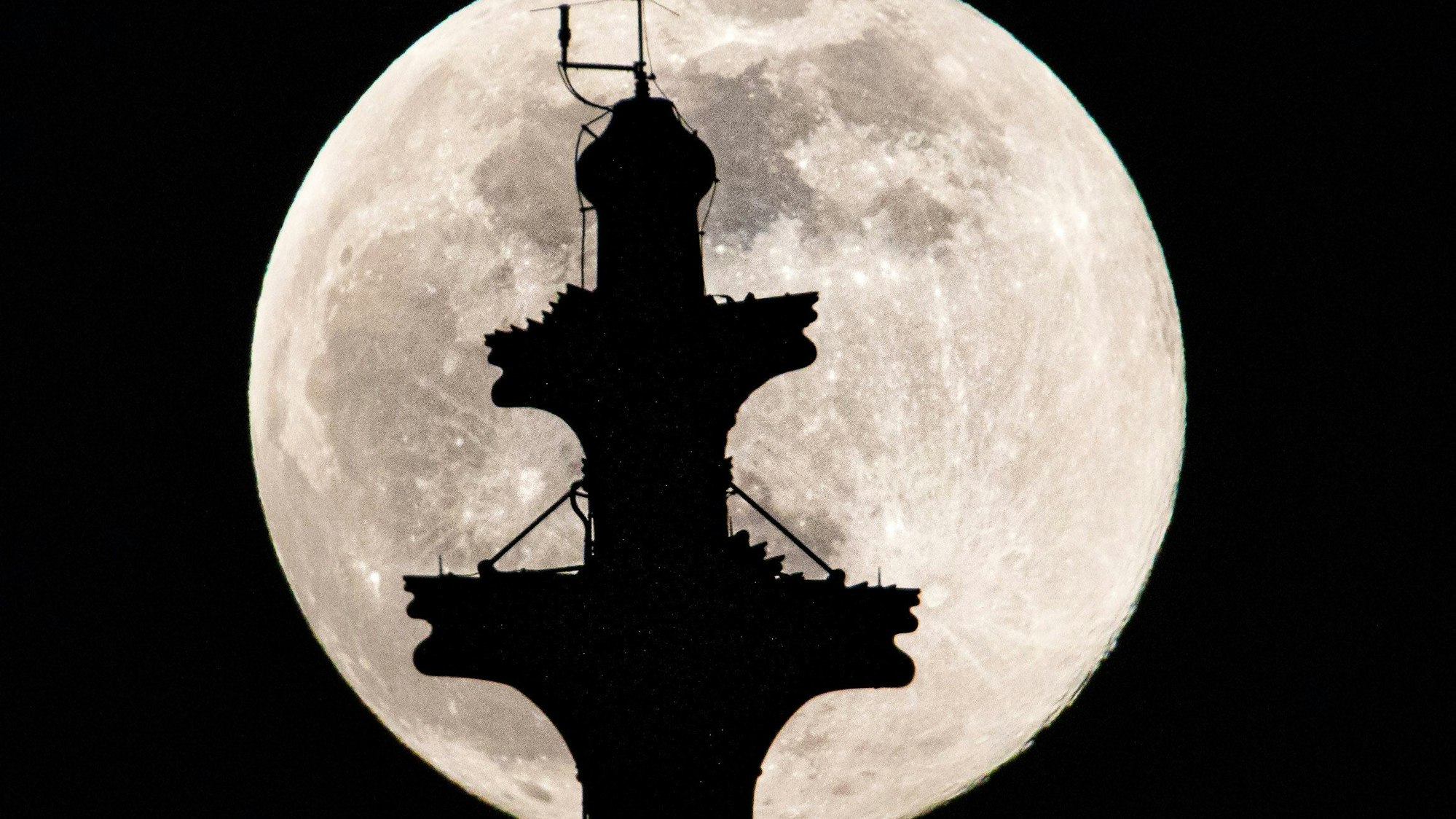 Der Vollmond steht hinter der Kreuzblume auf dem Nordturm des Kölner Doms.