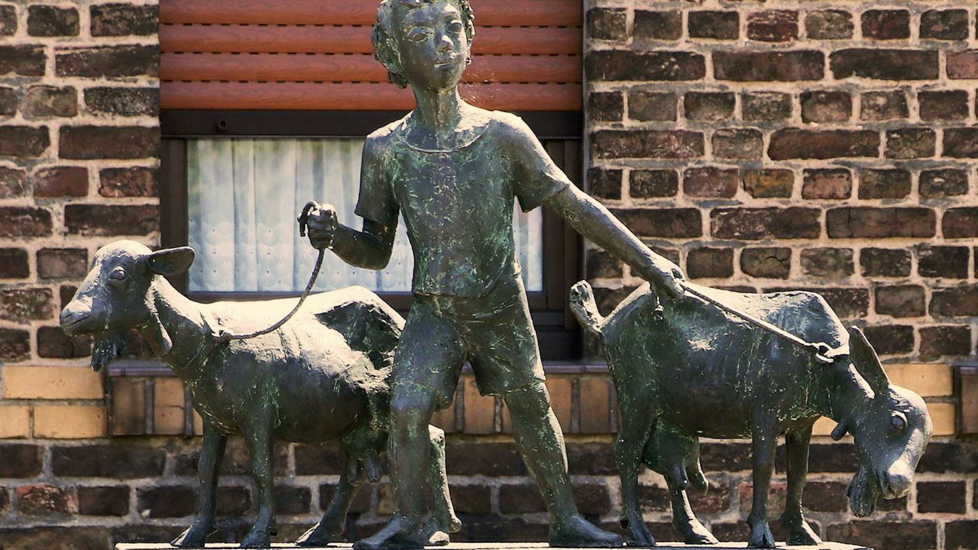 Eine Skulptur aus Bronze zeigt einen Jungen mit zwei Ziegen.