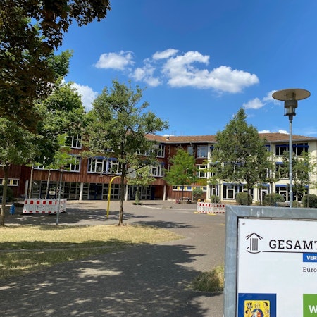 Das Foto zeigt die bestehende, von Bäumen umstandene Brühler Gesamtschule.