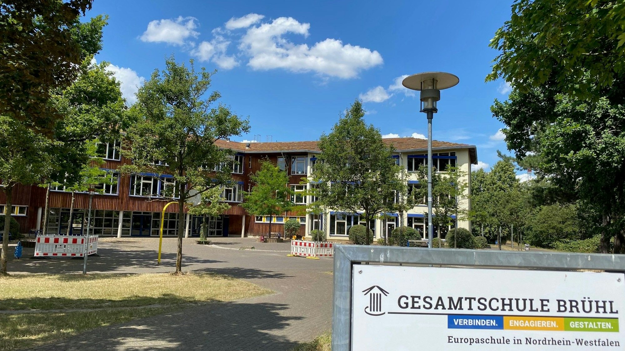 Das Foto zeigt die bestehende, von Bäumen umstandene Brühler Gesamtschule.