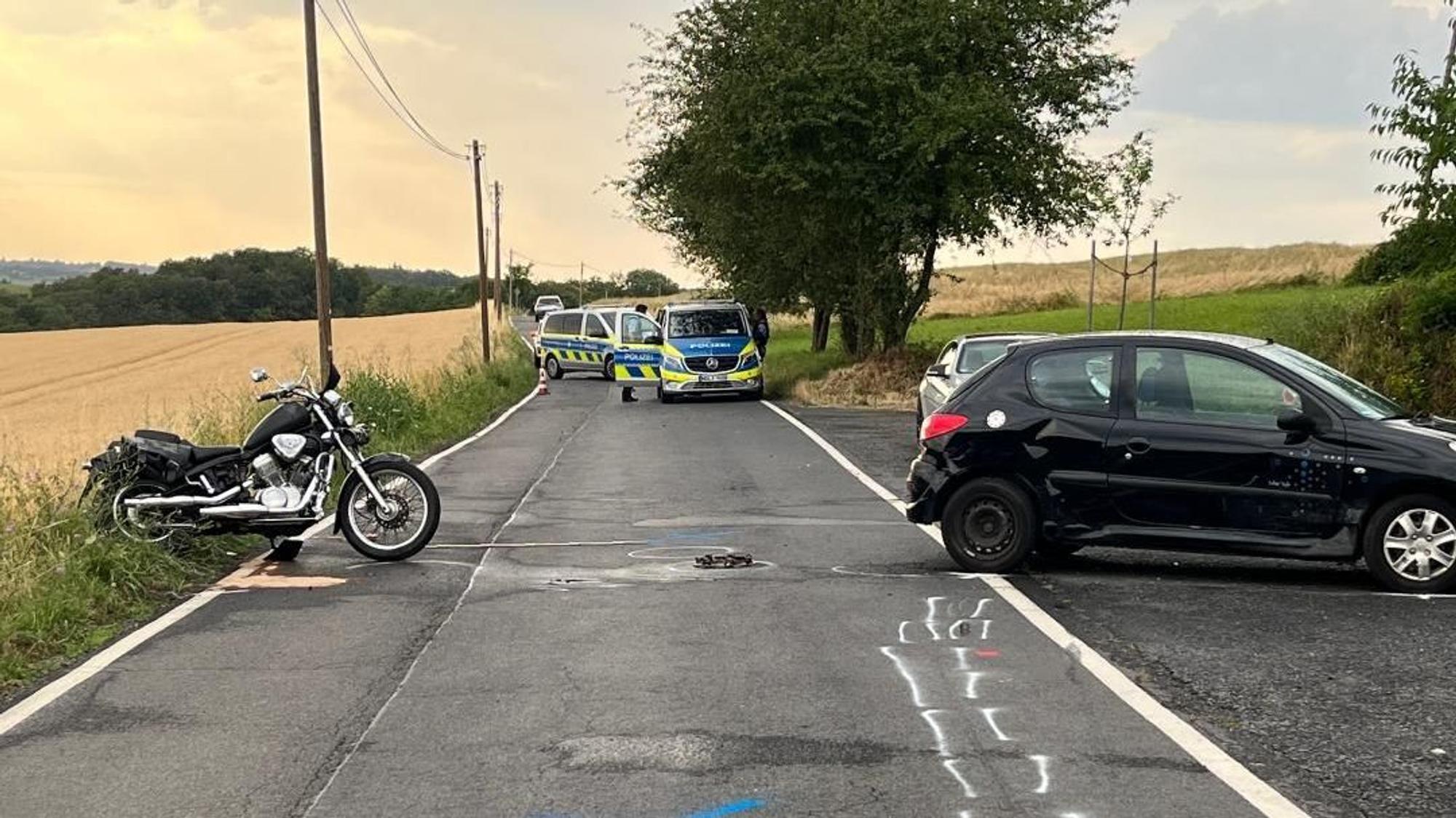 Ein Auto und ein Motorrad stehen nach einem Unfall auf einer Landstraße.