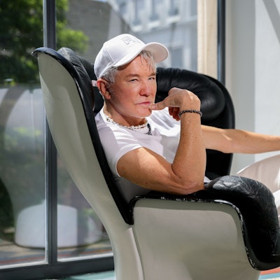 10.07.2023, Köln: Hollywood-Regisseur Baz Luhrmann sitzt in einem Drehsessel im Kölner Qvest-Hotel.
Er trägt eine weiße Baseball-Kappe, ein weißes T-Short und weiße Jeans.