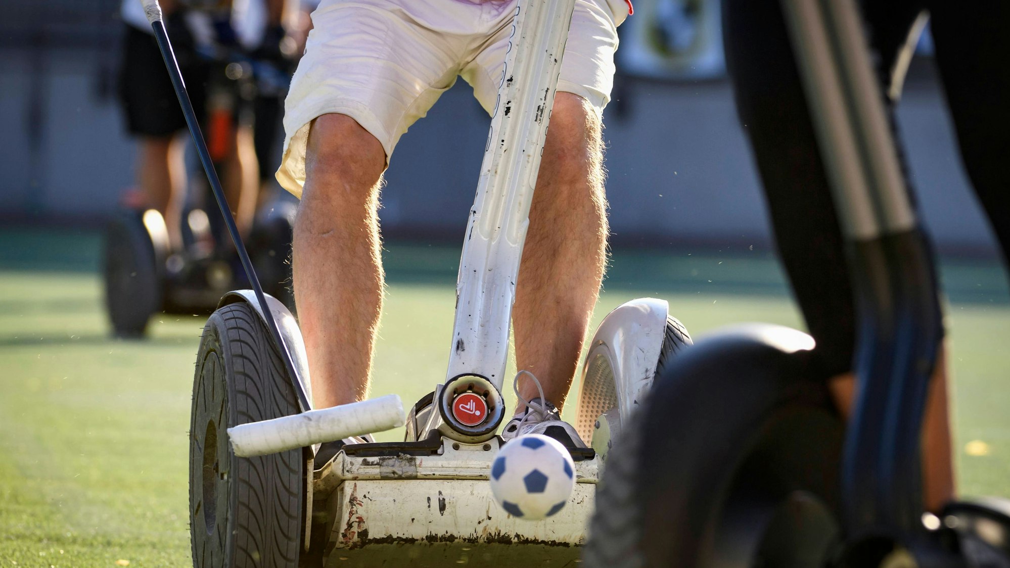 Zu sehen sind die Beine eines Mannes, der auf einem Segway steht und einen Polo-Schläger in der Hand hält.