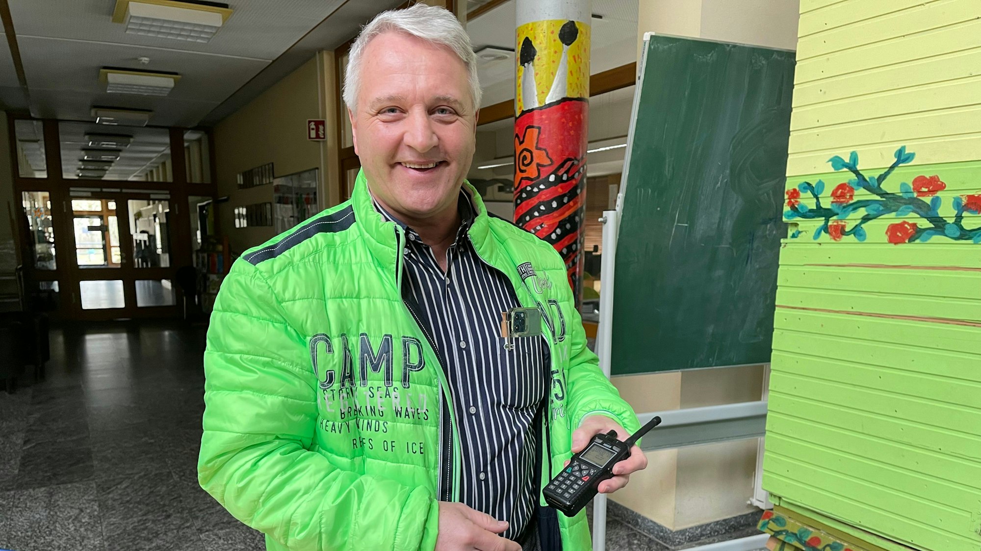 Ein Mann mit einer grünen Jacke hat ein Funkgerät in der Hand.