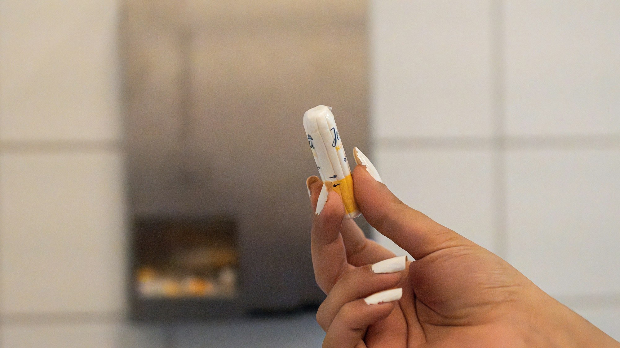 Eine Schülerin hält ein Menstruationsartikel vor einem Menstruationsartikel-Spender.