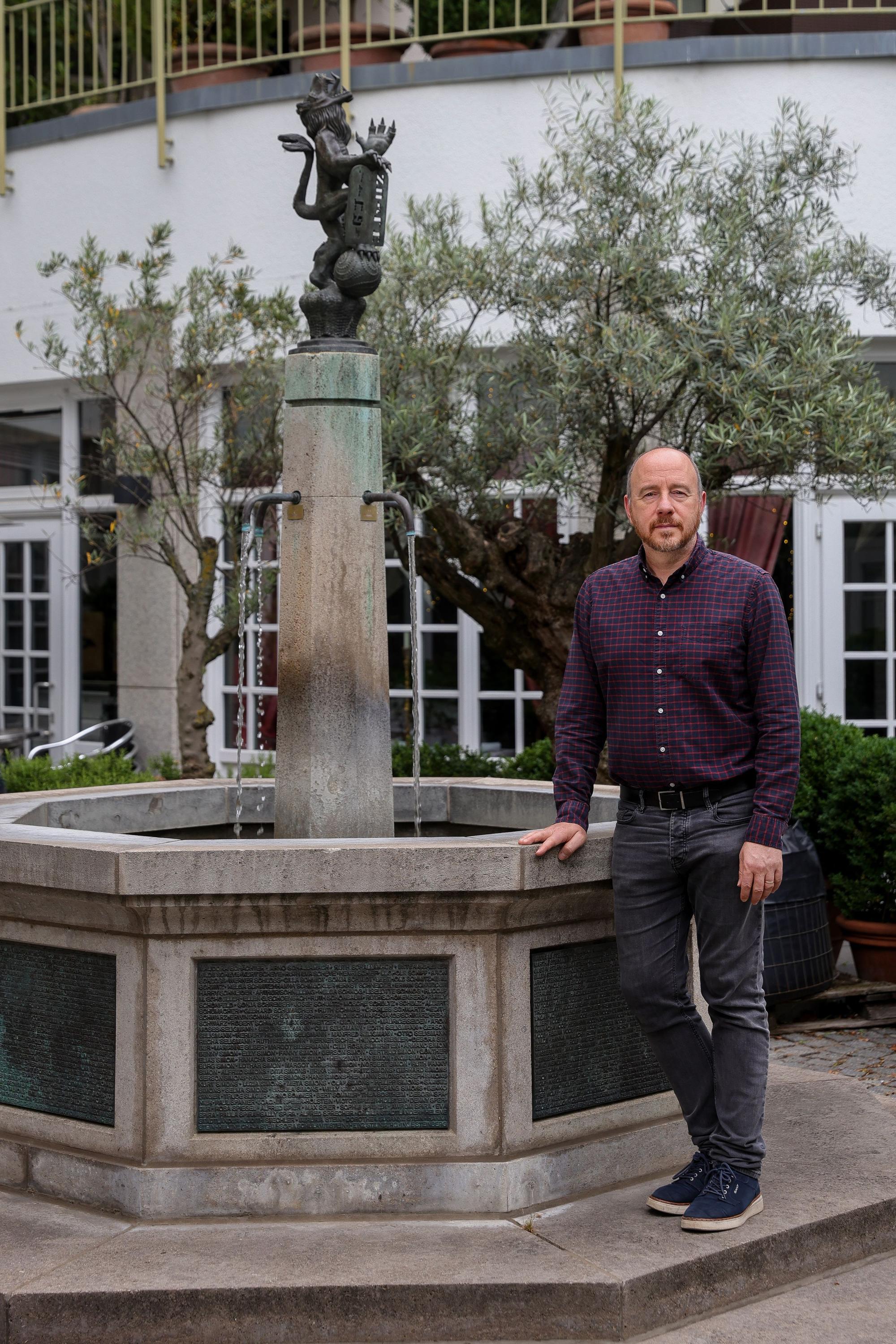 Aaron Knappstein lehnt die Hand an den Brunnen an und schaut in die Kamera.