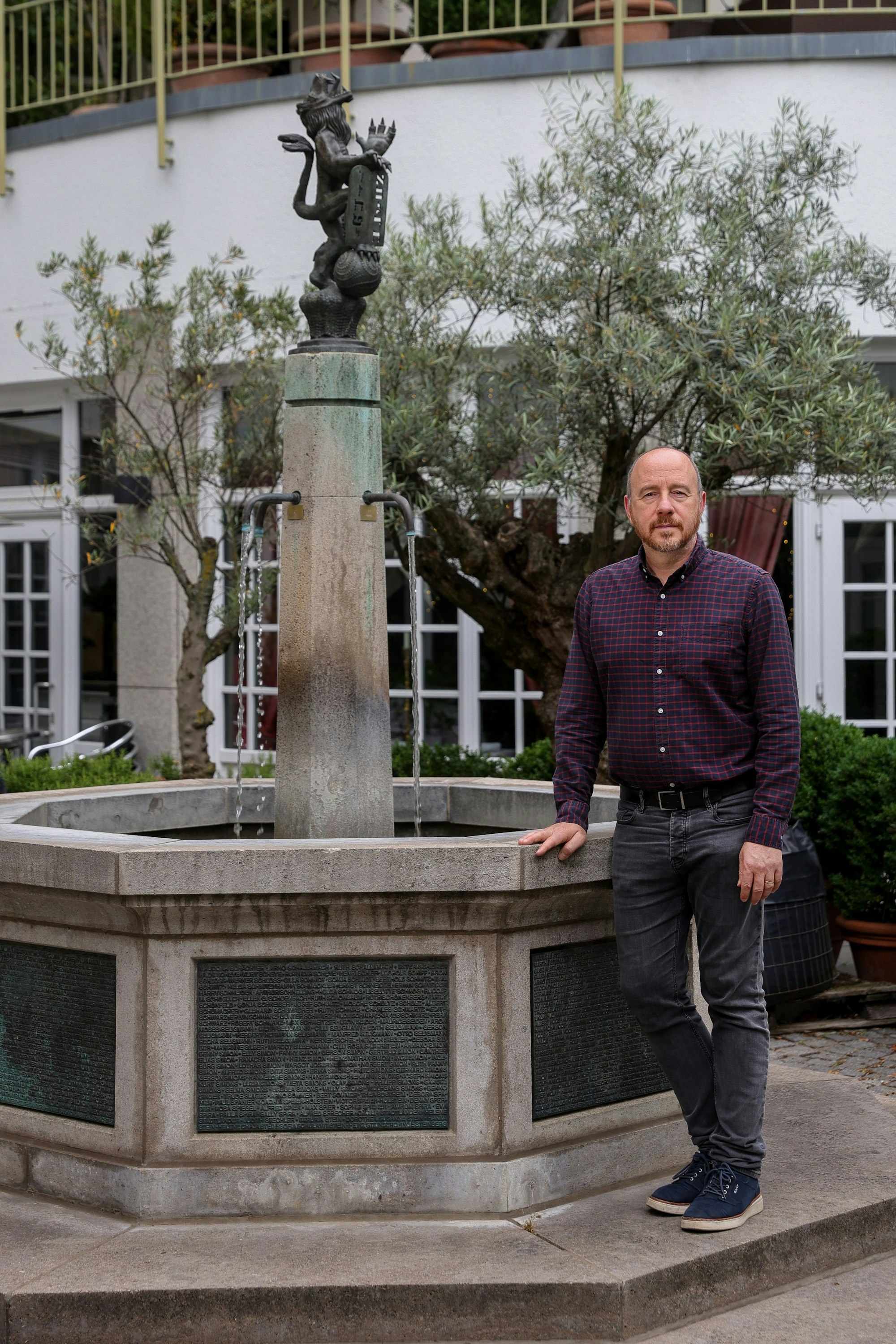 Aaron Knappstein lehnt die Hand an den Brunnen an und schaut in die Kamera.