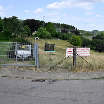 Eine grüne, eingezäunte Fläche mit Werbeschild. Im Hintergrund ein Trampolin.