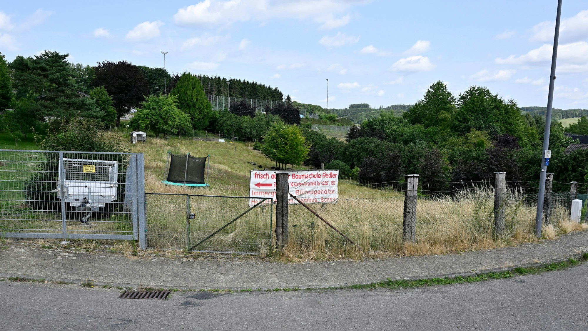 Eine eingezäunte Wiese mit einem Werbeplakat und einem Trampolin.